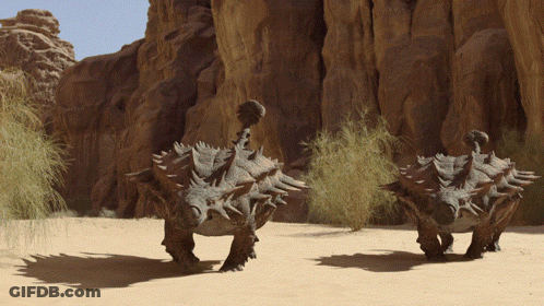 Dinosaurs Walking In Desert Near Rocks GIF