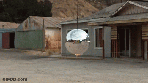 Disco Ball Hanging From Rope In Front Of Buildings GIF