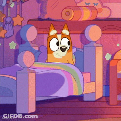 Dog Lying In Bed With Rainbow Blanket GIF