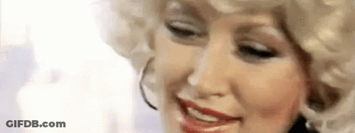 Dolly Parton Is Wearing A Blonde Wig And Hoop Earrings While Smiling . GIF