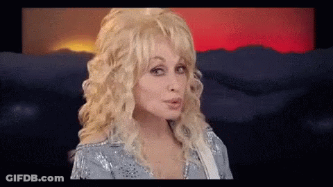 Dolly Parton Making Funny Face Holding Guitar In Front Of Mountains GIF