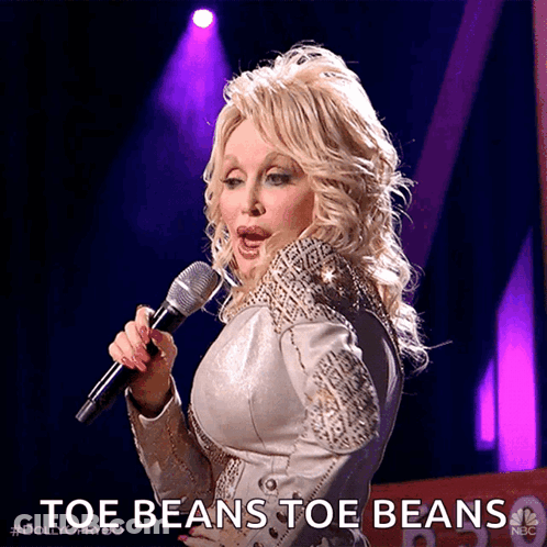 Dolly Parton Singing Into A Microphone With The Words Toe Beans Toe Beans Behind Her GIF