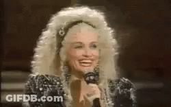 Dolly Parton Smiling Holding Microphone In Wig GIF