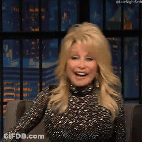 Dolly Parton Smiling In Chair In Front Of City Skyline GIF