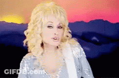 Dolly Parton Standing In Front Of Sunset Holding Guitar GIF