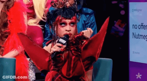 Drag Queen Holding Microphone In Front Of Nutmeg Sign GIF