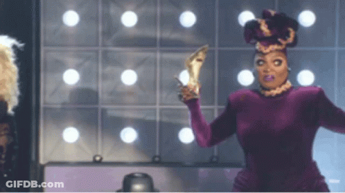 Drag Queen In Purple Dress Holding High Heels GIF