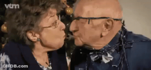 Elderly Couple Kissing In Front Of Christmas Tree GIF