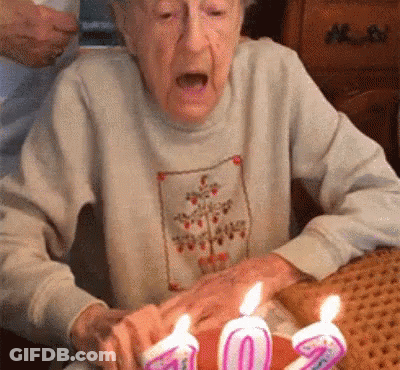 Elderly Woman Blowing Out Candles On Cake GIF