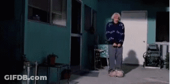 Elderly Woman Standing In Front Of Blue House GIF