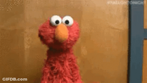 Elmo From Sesame Street Is Looking At The Camera While Standing In Front Of A Wall . GIF