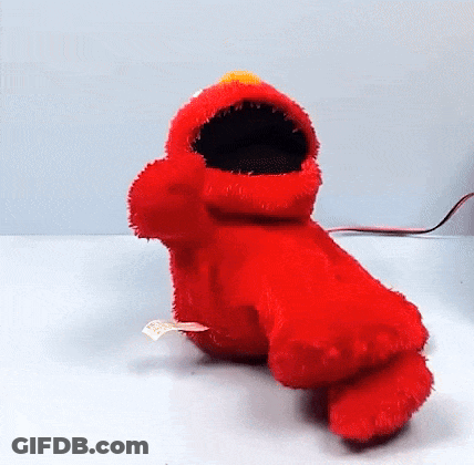 Elmo From Sesame Street Is Sitting On A Table With His Mouth Open And Looking At The Camera . GIF