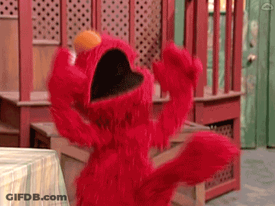 Elmo From Sesame Street Is Standing In Front Of A Table With His Mouth Open And His Arms Outstretched . GIF