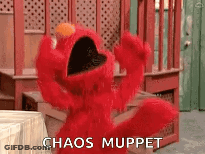 Elmo From Sesame Street Is Standing In Front Of A Table With His Mouth Open And Says `` Chaos Muppet '' . GIF