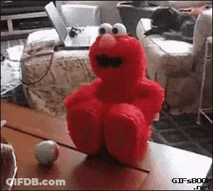 Elmo The Sesame Street Character Is Sitting On A Table With His Legs Crossed GIF