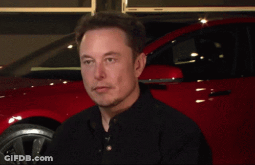 Elon Musk Is Smiling In Front Of A Red Car In A Garage GIF