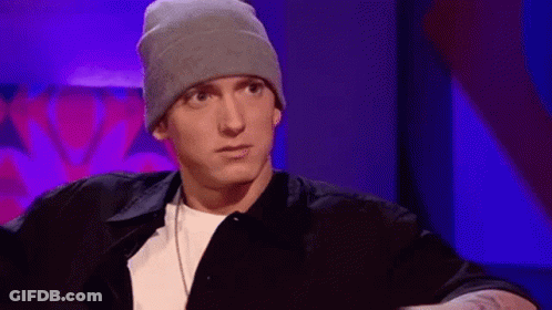 Eminem Is Wearing A Beanie And A Black Shirt While Sitting In A Chair . GIF