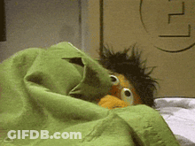 Ernie From Sesame Street Is Hiding Under A Green Blanket On A Bed GIF