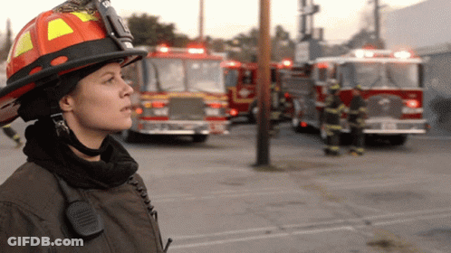 Female Firefighter With Helmet And Walkie Talkie In Front Of Fire Trucks GIF