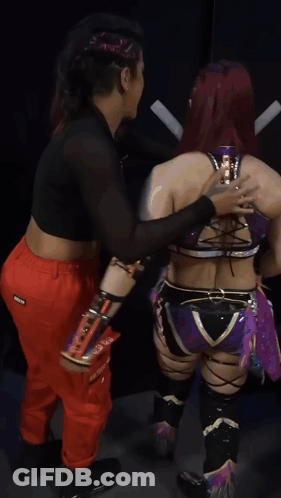 Female Wrestler Standing Next To Wrestler In Red Pants With X On Pocket GIF