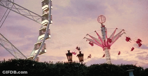 Ferris Wheel And Merry Go Round Against Pink Sky GIF