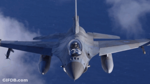 Fighter Jet Flying Through Cloudy Blue Sky With Flag In Cockpit GIF