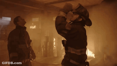 Fireman Holding Hose In Front Of Burning Building GIF
