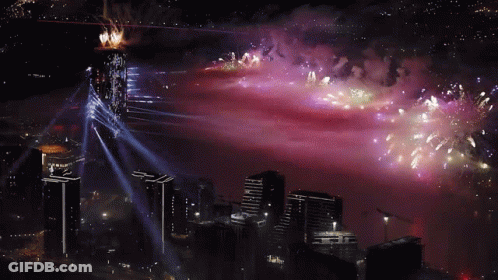 Fireworks Are Displayed Over A City With A Purple Sky In The Background GIF