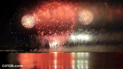 Fireworks Display Over A Body Of Water With A City In The Background GIF