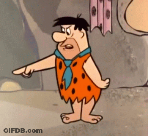 Flintstone From The Flintstones Is Standing In Front Of A Rock Wall And Pointing At Something . GIF