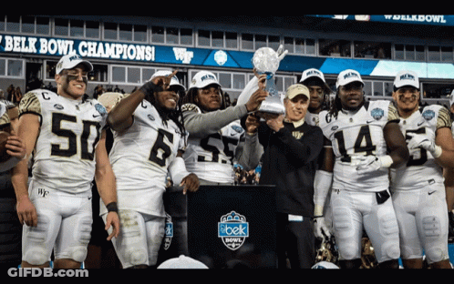Football Players Holding Trophy In Front Of Belk Bowl Sign GIF