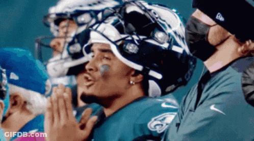 Football Players Sitting In Row With Masked Man GIF