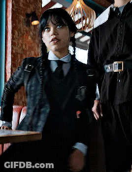 Girl In Black Jacket And Tie Sitting At Table GIF