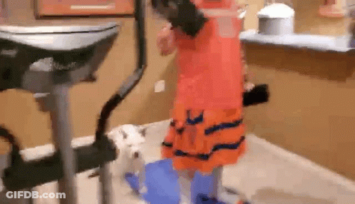 Girl In Orange Dress Standing By Dog On Exercise Bike GIF