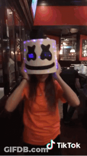 Girl In Orange Shirt With Lit Marshmello Hat GIF