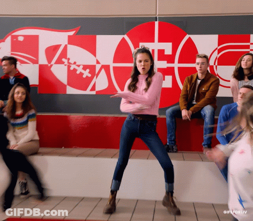 Girl In Pink Sweater Dancing In Front Of Football Wall GIF