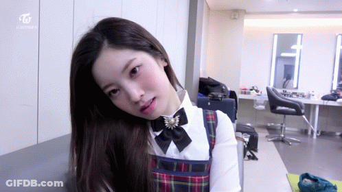 Girl In Plaid Dress Sitting In Room With Twice On Wall GIF