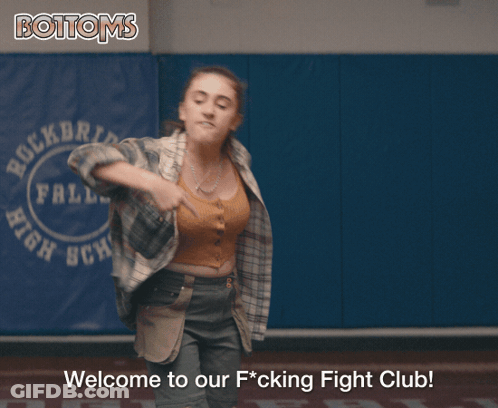 Girl In Plaid Shirt Next To Bottoms Sign GIF