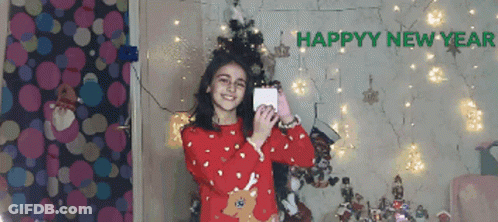 Girl In Red Sweater Taking Selfie In Front Of Happy New Year Sign GIF