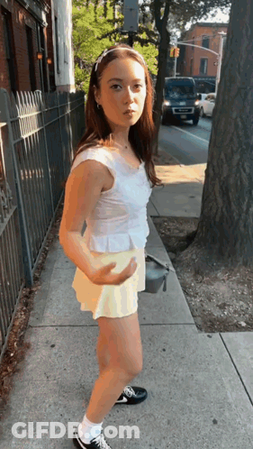 Girl In White Top And Yellow Shorts On Sidewalk GIF
