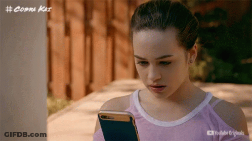 Girl Looking At Cell Phone With Cobra Kai Logo GIF