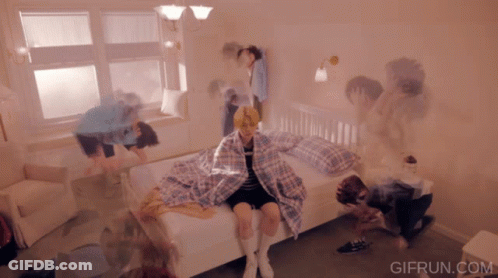 Girl Sitting On Bed Surrounded By People GIF