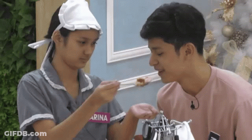 Girl With Arina On Shirt Feeds Boy GIF