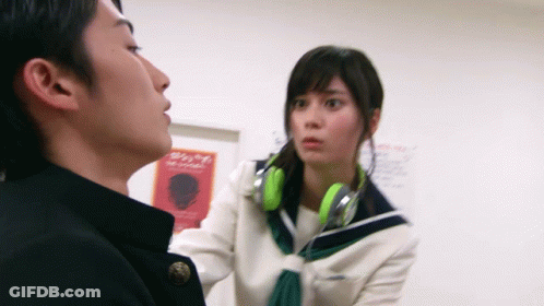 Girl With Green Headphones Talks To Boy In Front Of Sign Saying A GIF
