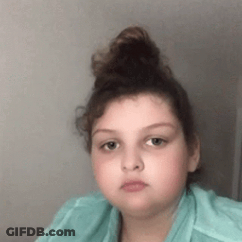 Girl With Hair Bun In Green Shirt Looking At Camera GIF