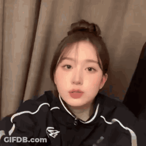 Girl With Hair Bun Sitting In Front Of Curtain GIF