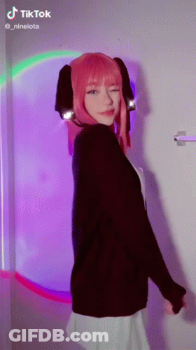 Girl With Pink Hair Standing In Front Of Rainbow Wall GIF