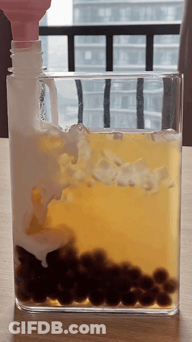 Glass Container With Yellow Liquid And Black Balls GIF