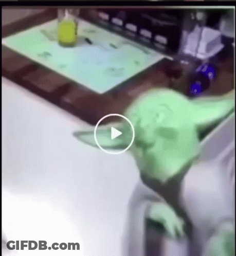 Green Alien Laying On Table With Play Button GIF