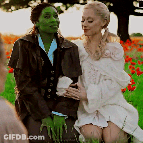 Green And Blonde Women In Costumes Sitting In Flowers GIF